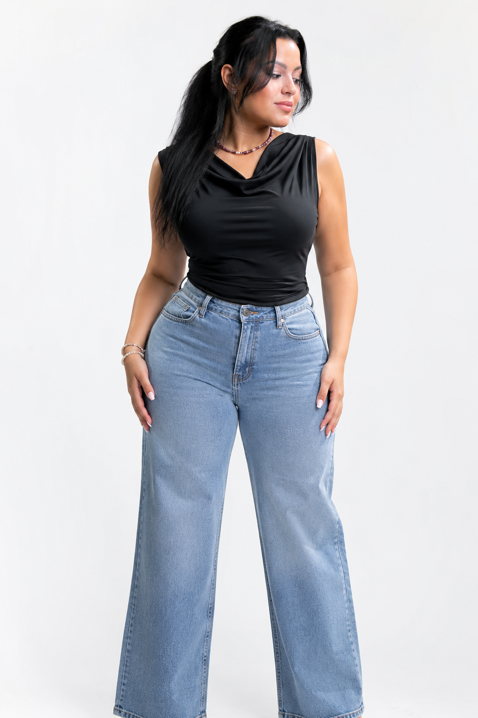 Woman wearing a black sleeveless top and blue jeans on a white background