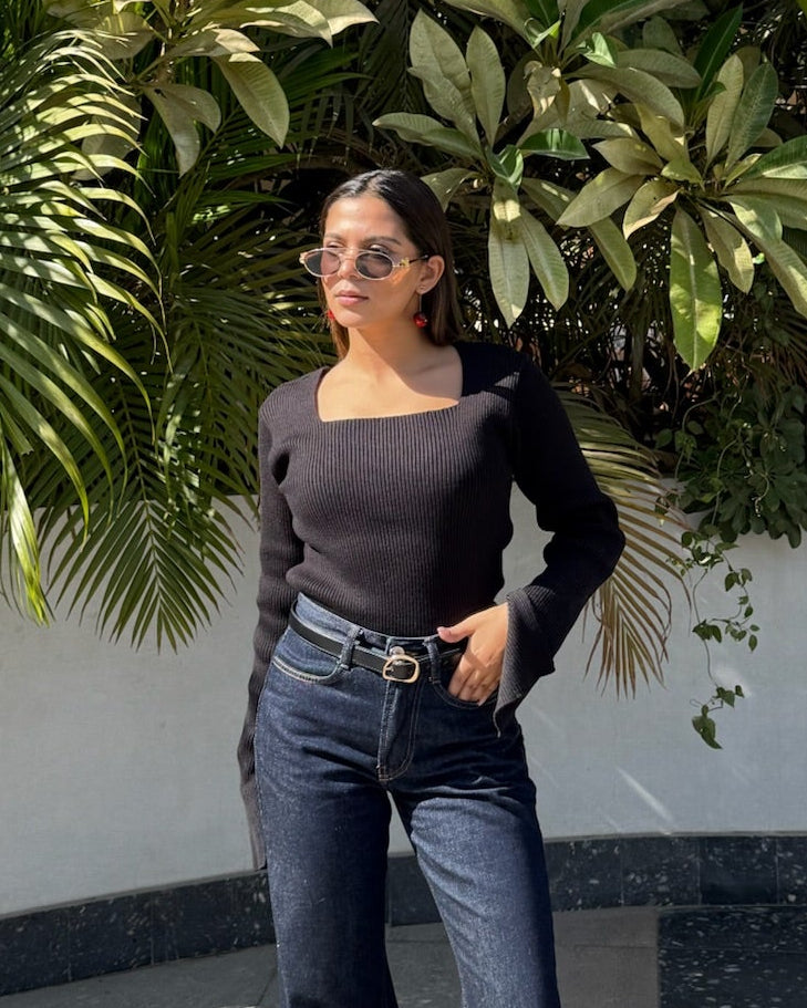 A female standing in a lush green indoor garden wearing a black knit top